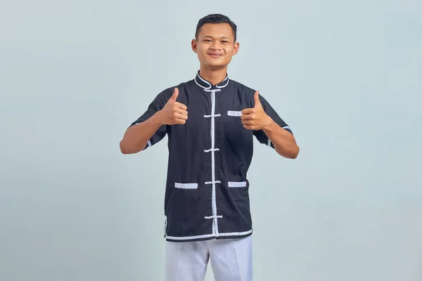 笑顔の肖像アジアの若い男は 空手を着て親指を表示または灰色の背景に承認サイン — ストック写真