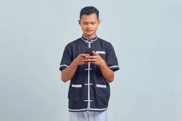 灰色の背景に携帯電話を使用して空手の制服を着て悲しいアジアの若者の肖像画 — ストック写真