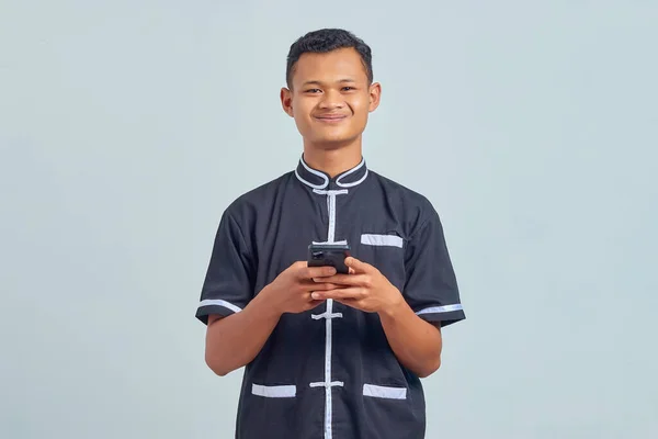 笑顔の肖像アジアの若い男は灰色の背景に携帯電話を使用して空手の制服を着て — ストック写真