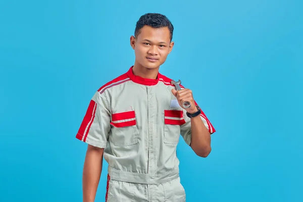 青い背景に隔離された機械的な均一な保持レンチを身に着けているアジアのハンサムな男の笑顔のイメージ — ストック写真
