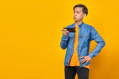 Asyalı adam sarı arka planda kızgın yüzlü cep telefonu oyunu oynuyor
