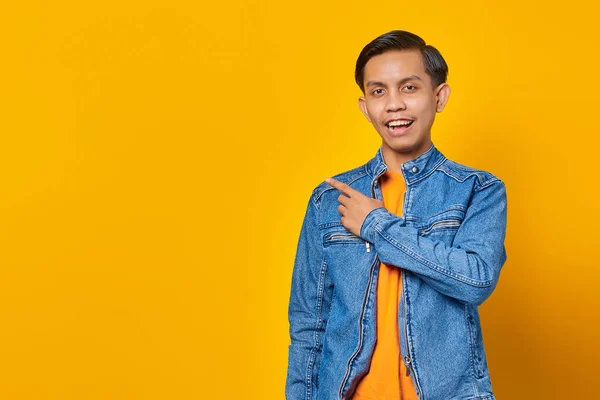 Portrait of a cheerful and excited Asian man pointing to an empty space isolated on yellow background