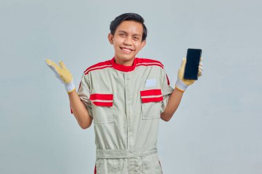 Tamirci üniforması giyen yakışıklı bir adamın portresi ve gri arka planda başarıyı kutluyor.