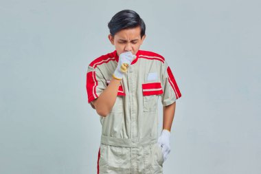 Tamirci üniforması giyen yakışıklı adam kendini iyi hissetmiyor ve öksürüyor. Soğuk algınlığı ya da bronşit belirtileri var.