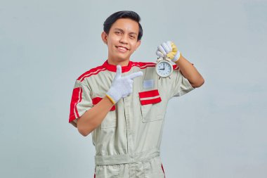 Mekanik üniforma giyen gülümseyen yakışıklı adamın portresi gri arka planda çalar saat tutuyor.