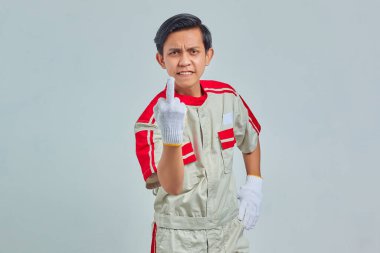 Mekanik üniforma giyen, gri arka planda orta parmağını kameraya gösteren sinirli yakışıklı bir adam portresi.