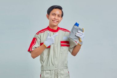 Motor yağı şişesini gri arka planda gösteren mekanik üniforma giyen gülümseyen yakışıklı adamın portresi.