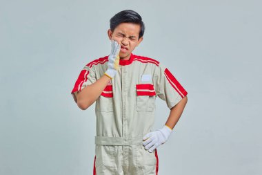 Mekanik üniforma giyen yakışıklı bir adamın portresi. Gri arka planda acı dolu bir ifadeyle dudaklara dokunuyor.