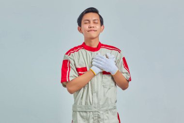 İki eli göğsünde gri arka planda tamirci üniforması giyen yakışıklı bir adam portresi.