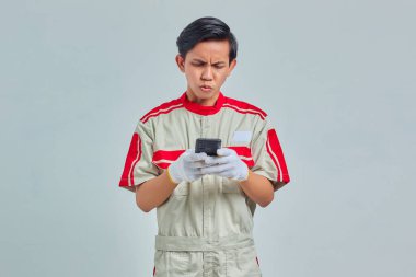 Mekanik üniforma giyen heyecanlı yakışıklı adam gri arka planda izole cep telefonu kullanıyor.