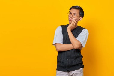 Şok olmuş Asyalı genç adam sarı arka planda izole edilmiş boş bir alana bakıyor.