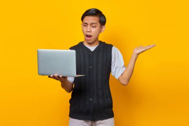 Şok olmuş genç adam gelen e-postaya bakıyor ve sarı arka planda dizüstü bilgisayarı tutuyor.