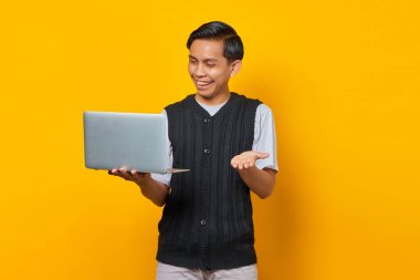 Mutlu yakışıklı iş adamı dizüstü bilgisayara bakıyor ve sarı arka planda elini kaldırıyor.