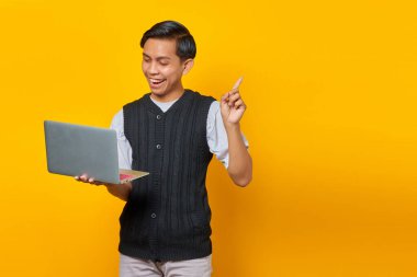 Sarı arka planda dizüstü bilgisayar tutarken yaratıcı bir fikri olan heyecanlı genç iş adamı.