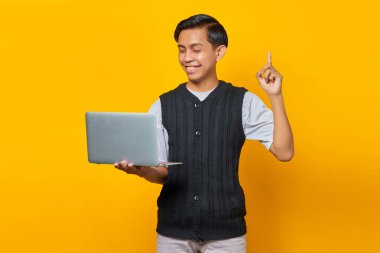 Sarı arka planda dizüstü bilgisayar tutarken yaratıcı bir fikri olan heyecanlı genç iş adamı.