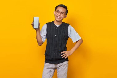 Gülümseyen genç yakışıklı adam sarı arka planda elinde akıllı telefon boş ekranını gösteriyor.