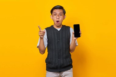 Şaşırmış Asyalı adam boş akıllı telefon ekranı ve boş yeri işaret ediyor.