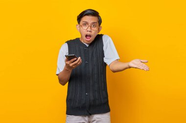 Asyalı öfkeli bir gencin portresi. Elinde cep telefonu var. Sarı arka planda.