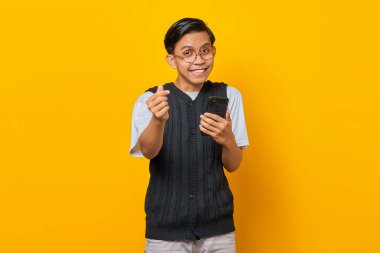 Neşeli Asyalı bir gencin portresi. Parmağını gösteren ve elinde akıllı telefon tutan.