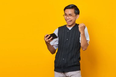 Cep telefonunda video oyunu oynayan ve başarıyı kutlayan neşeli Asyalı genç adamın portresi