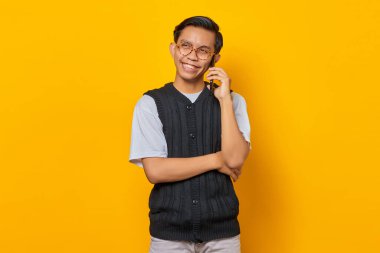 Sarı arka planda cep telefonuyla konuşan mutlu Asyalı adamın portresi