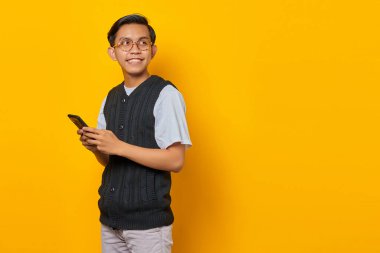 Akıllı telefonu tutan ve sarı arka plana bakan neşeli genç yakışıklı adam.