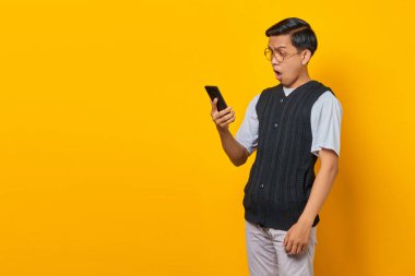 Akıllı telefona bakan heyecanlı Asyalı adam sarı arka plandan iyi haberler alıyor.