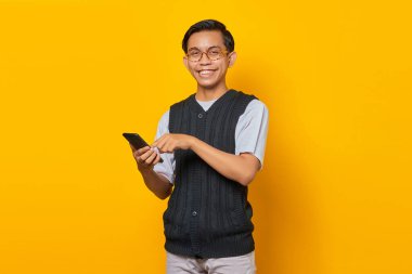 Sarı arka planda akıllı telefon kullanan ve mesajlaşan neşeli yakışıklı genç adam.