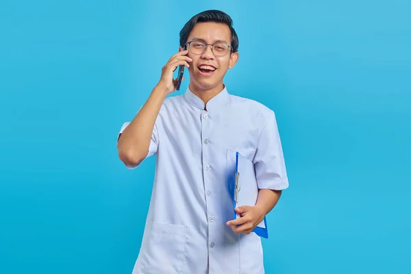 陽気なハンサムな男性看護師保持クリップボードと話上の携帯電話上の黄色の背景 — ストック写真