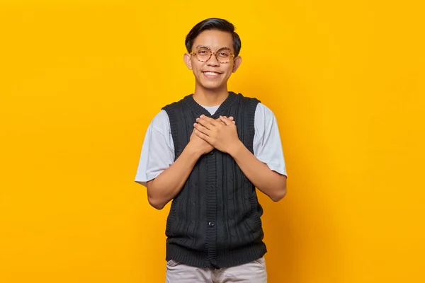 Щасливий Молодий Азіат Тримає Обидві Пальми Грудях Ізольованими Жовтому Фоні — стокове фото