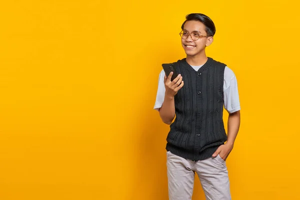 笑顔若いですアジアの男話しています携帯電話と見下ろし以上黄色の背景 — ストック写真