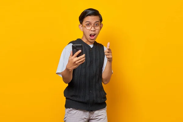 Здивований Молодий Азіат Тримає Мобільний Телефон Вказує Пальцем Камеру Жовтому — стокове фото