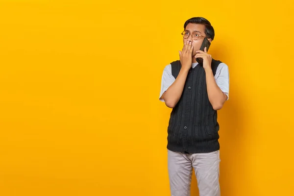 Sorprendido Joven Asiático Hablando Teléfono Inteligente Cubriendo Boca Fondo Amarillo — Foto de Stock