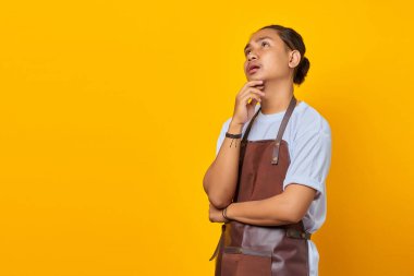 Çekici yakışıklı barista, çenesini kaldırmış, elini kaldırmış ve sarı arka planda izole bir şekilde yukarı bakıyor.