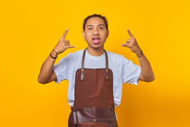 Önlük giymiş yakışıklı Asyalı genç adamın portresi çılgın bir ifadeyle çığlık atıyor elleri havada rock sembolü yapıyor. 