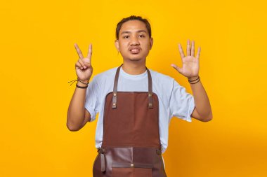 Önlük giymiş yakışıklı Asyalı genç adamın portresi kızgın ifadeyle yedi numaralı parmağı işaret ediyor.