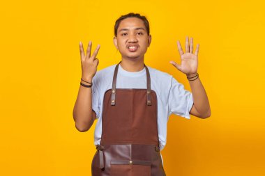 Önlük giymiş yakışıklı Asyalı genç bir adamın portresi kızgın bir ifadeyle sekiz numarayı işaret ediyor.