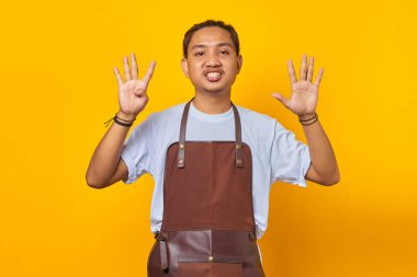 Önlük giymiş yakışıklı Asyalı genç bir adamın portresi. Sinirli bir ifadeyle dokuz numarayı işaret ediyor.