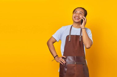 Gülümseyen ve neşeli Asyalı genç adamın portresi sarı arka planda akıllı telefondan konuşuyor.