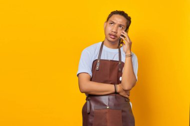 Sarı arka planda akıllı telefondan aranan mutsuz Asyalı genç adamın portresi