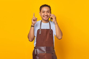 Akıllı telefondan konuşan ve parmağı havada gülümseyen Asyalı genç adamın portresi. sarı arkaplan