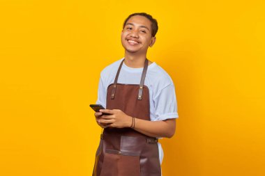 Neşeli, yakışıklı bir baristanın portresi. Önüne bakıyor ve sarı arka planda akıllı telefonu tutuyor.