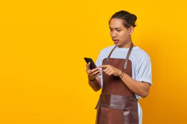 Önlük giymiş Asyalı genç adamın portresi sarı arka planda akıllı telefondan gelen mesajı görünce şaşırdı.