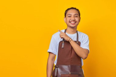 Önlük takmış gülümseyen Asyalı bir gencin portresi sarı arka planda parmağıyla fotokopi alanını işaret ediyor.