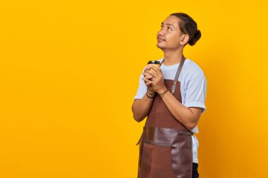 Kağıt bardak tutan neşeli, pozitif, yakışıklı bir adamın portresi ve sarı arka planda boş bir alana bakıyor.