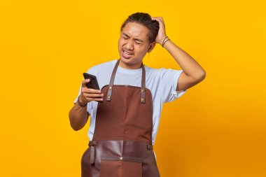 Akıllı telefonu tutan yakışıklı Asyalı adamın portresi kafasına dokunuyor ve sarı arka planda endişelerini dile getiriyor.