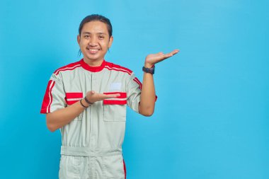 Mekanik üniforma giyen neşeli yakışıklı adamın portresi mavi arka planda avuç içinde fotokopi alanı gösteriyor.