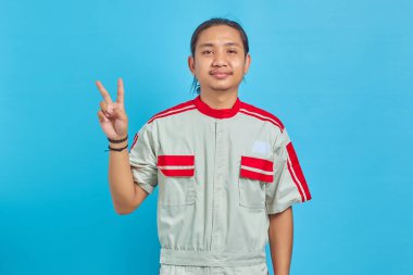 Mavi arka planda barış işareti gösteren, mekanik üniforma giyen gülümseyen yakışıklı adamın portresi.