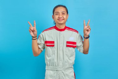 Mavi arka planda barış işareti gösteren, mekanik üniforma giyen gülümseyen yakışıklı adamın portresi.