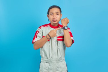 Mekanik üniforma giyen kızgın yakışıklı adamın portresi mavi arka plandaki saati kontrol ediyor.